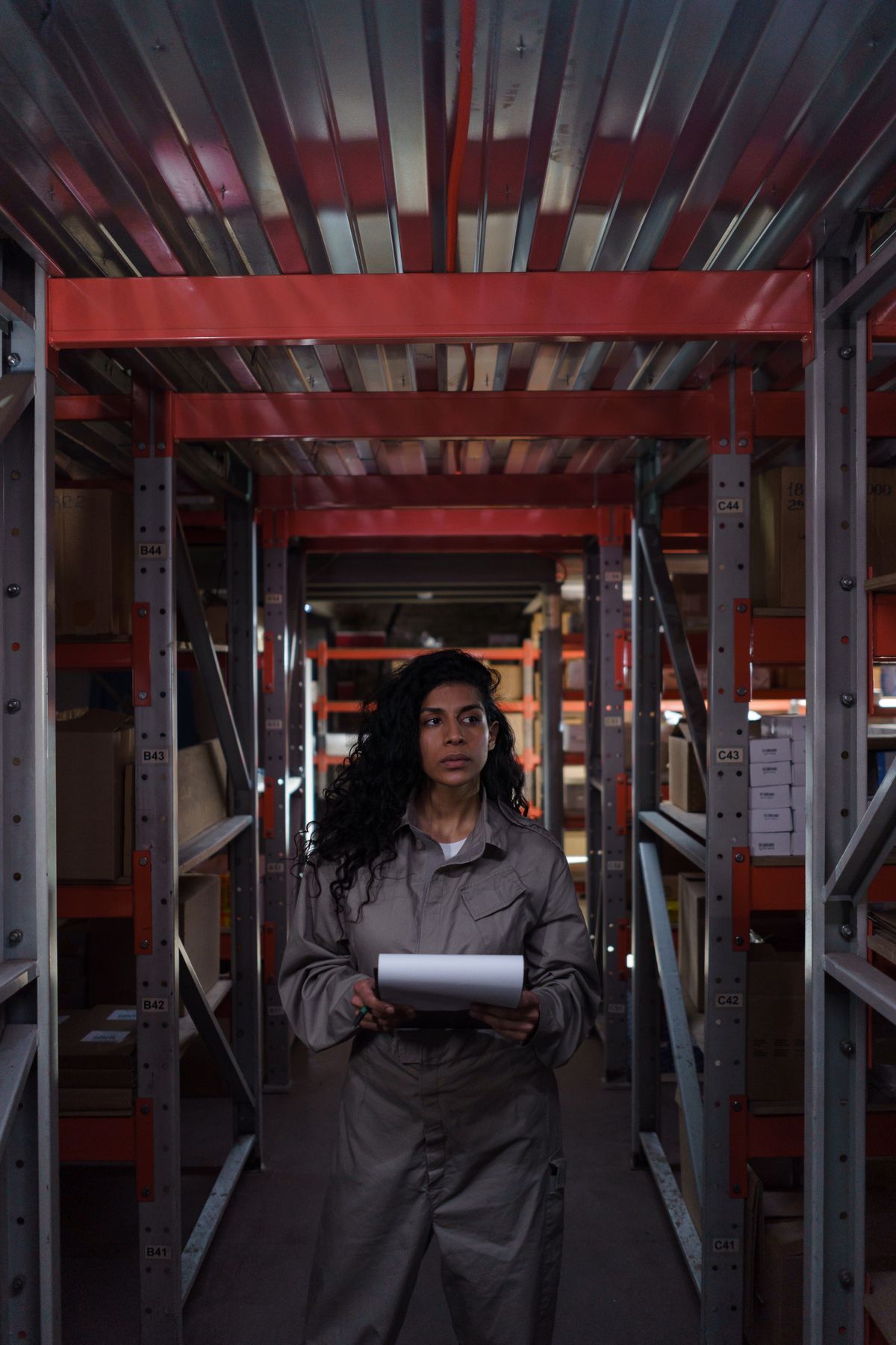 Warehouse staff member checking inventory records among storage racking