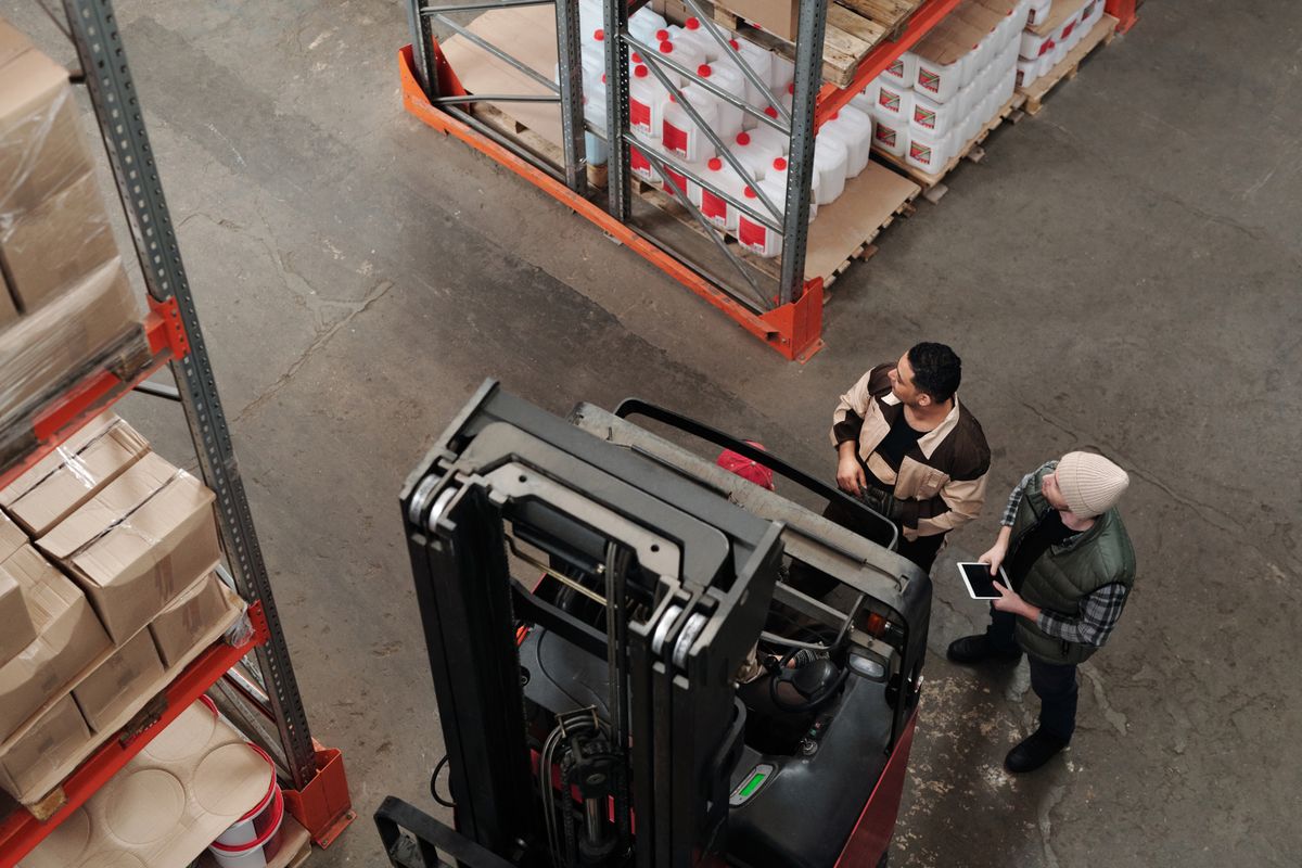 Warehouse staff coordinating a forklift delivery among stocked pallets